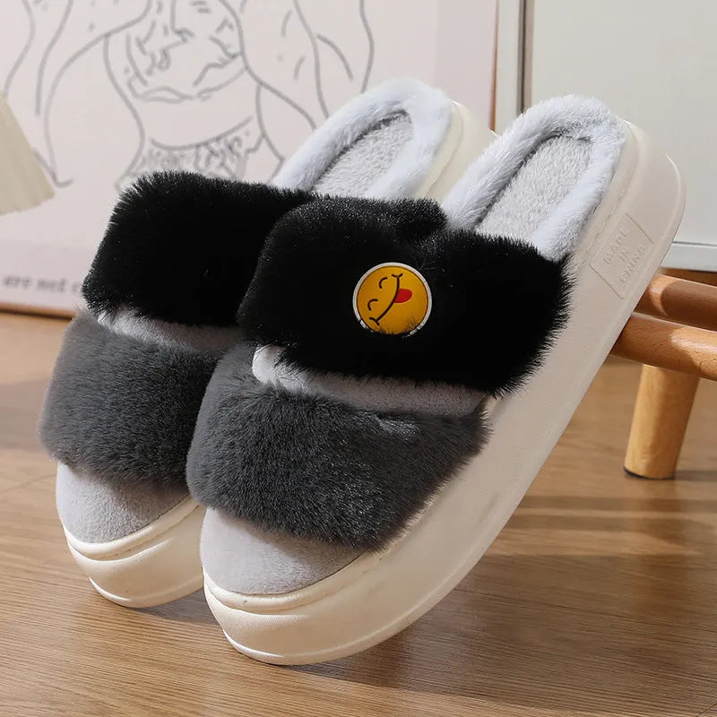 A pair of pink and green thermal plush slippers with a cashmere lining, shown on a wooden floor.