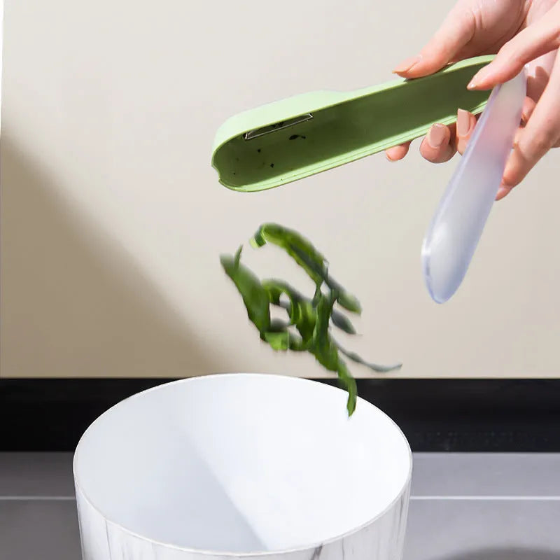 Dark green kitchen peeler with storage tube, non-slip handle, and stainless steel blade on a kitchen counter.