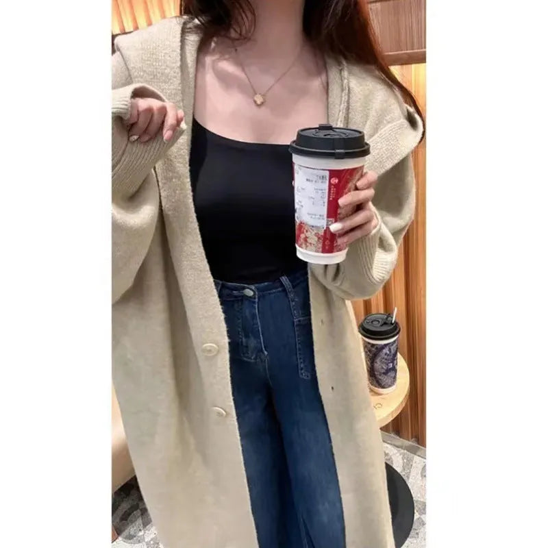Long beige hooded knitted cardigan on a woman, showcasing its below-the-knee length and loose fit.