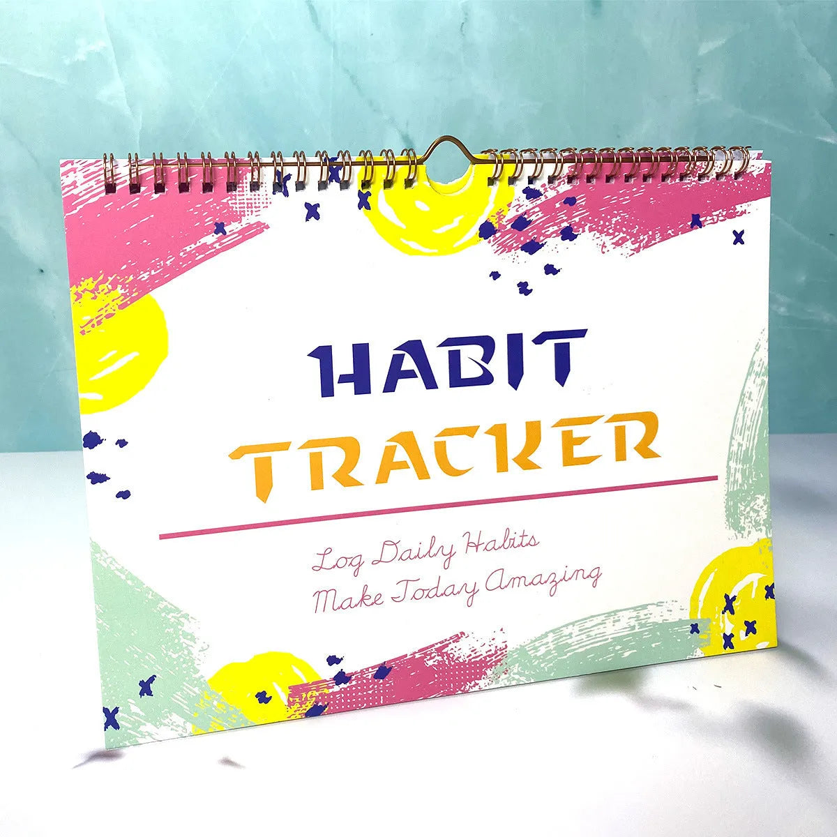 A5 habit tracking notebook open on a desk, showing internal pages, available in four colour options.