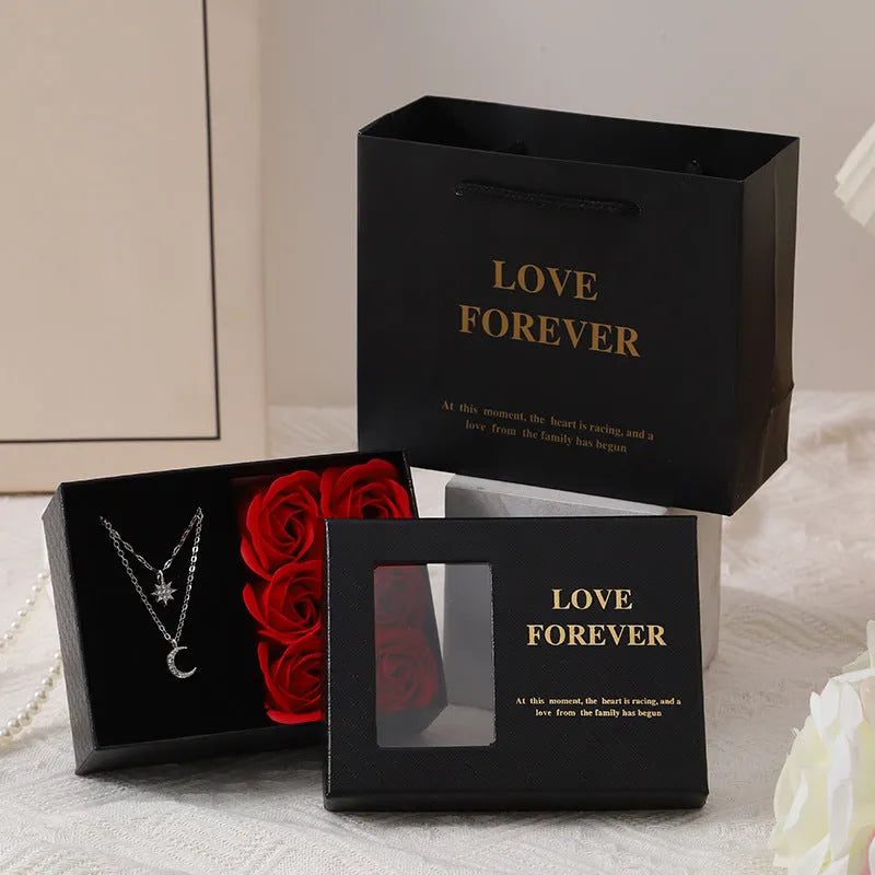 Red Valentine's gift box containing six pink soap flowers, with a matching red handbag alongside.