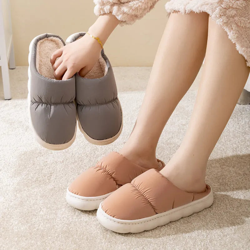 A pair of blue down cotton winter slippers with a thick rubber sole and plush lining on a wooden floor.