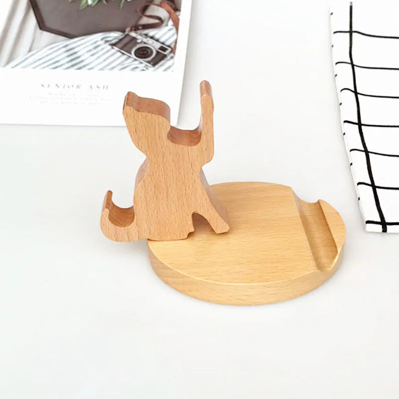 Solid beech wood mobile phone stand with a resin cow figurine and a slot for holding coins on a wooden desk.