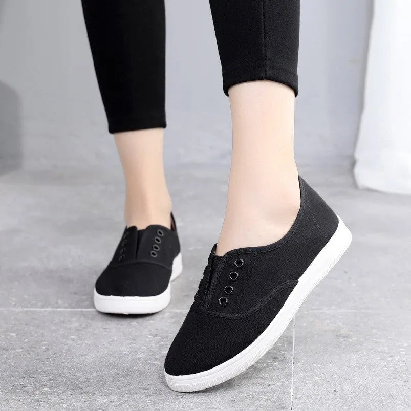 A pair of low-top casual canvas shoes in a flat style, shown in a choice of colours including black, white, grey, and pink.
