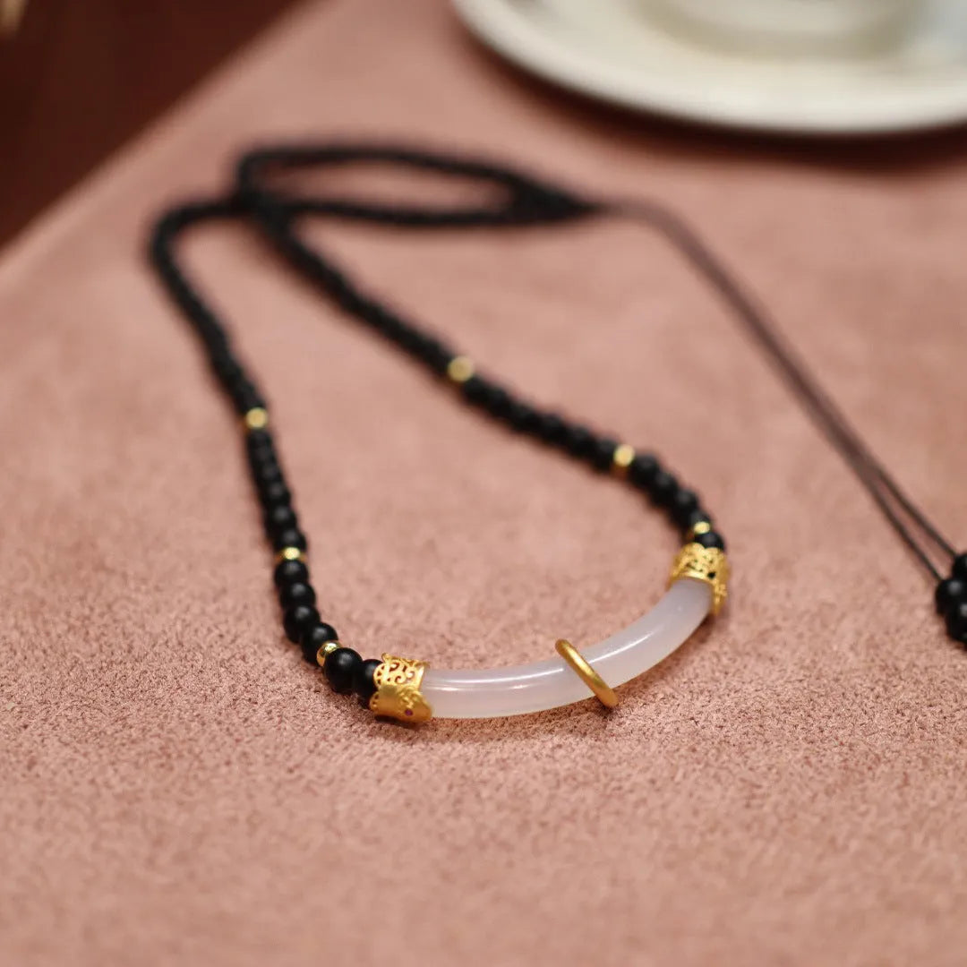 Close-up of a Chinese style U-shaped necklace with a frosted black agate and white chalcedony pendant on a silver ball bead chain.