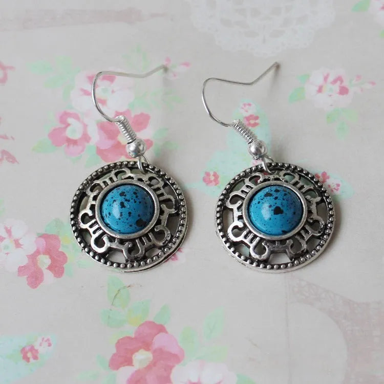 Handmade geometric silver earrings with turquoise flower disk and ethnic patterns in red, blue, or black.