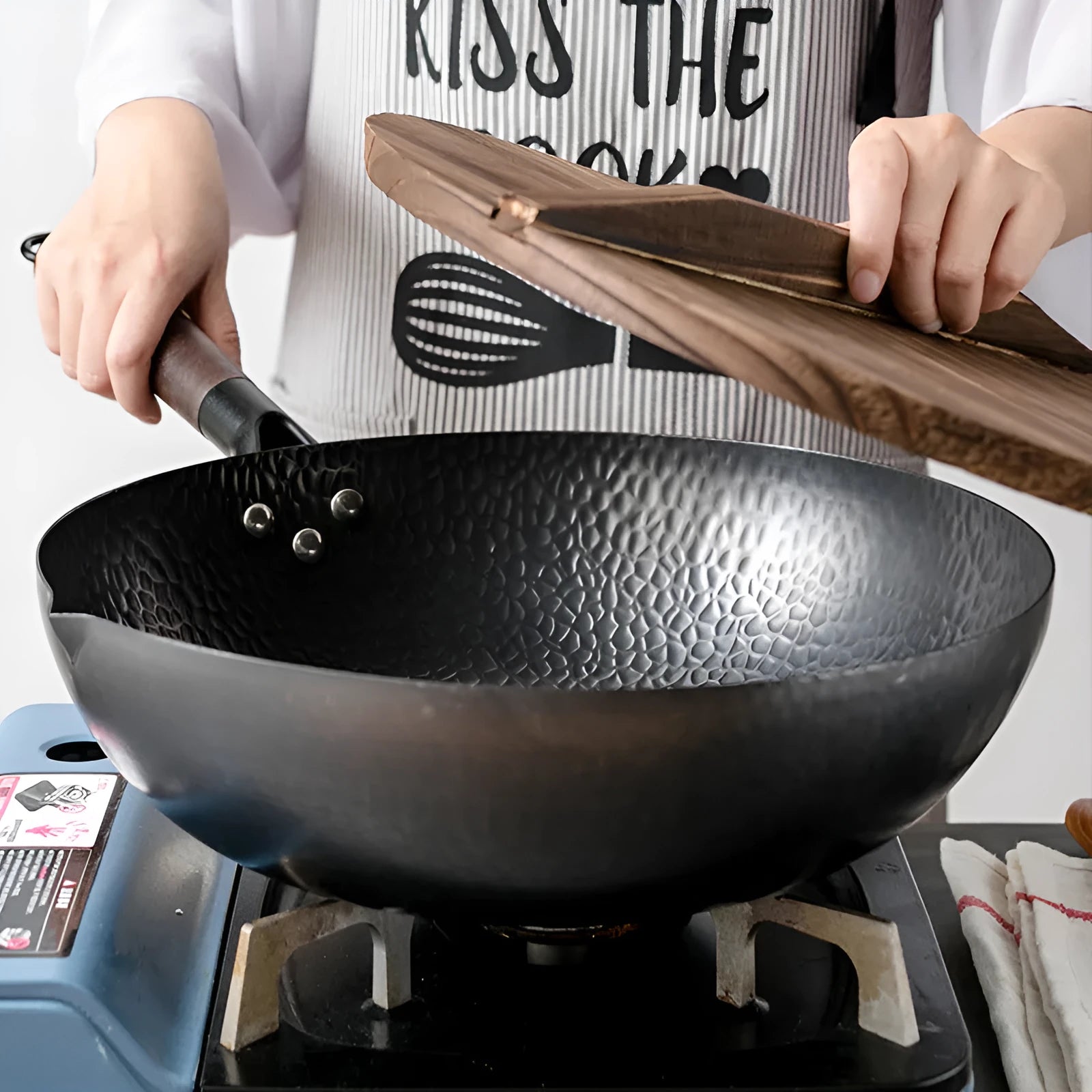 Black handmade traditional iron wok with a long wooden handle, shown with a glass lid.