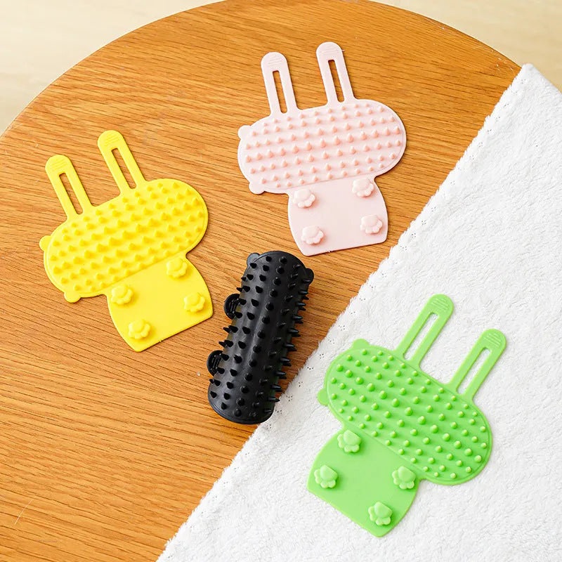 Silicone cat grooming comb with rounded teeth and adjustable strap mounted on a table leg.