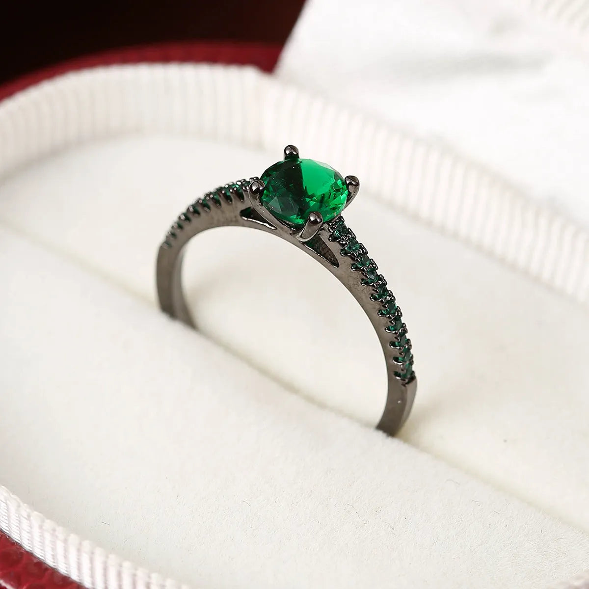 A hexagonal geometric ring with a zircon stone, shown in a gun black and rose red electroplated finish on a finger.
