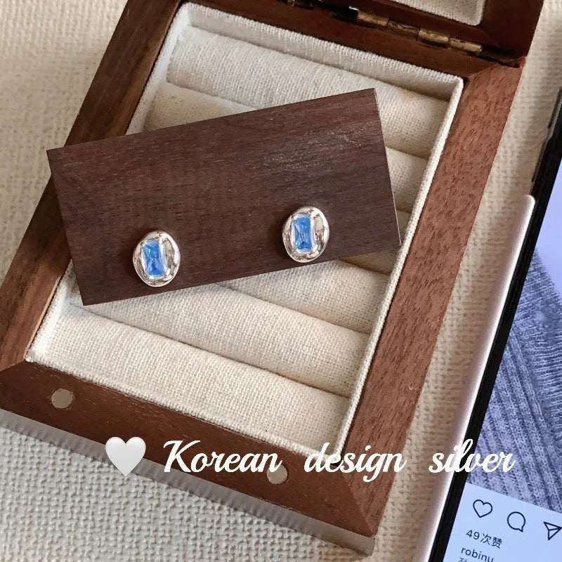 Women's sterling silver earrings with oval heart-wrapped design and blue diamond accents