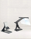 Black foldable mobile phone screen amplifier and detachable holder set up on a desk.