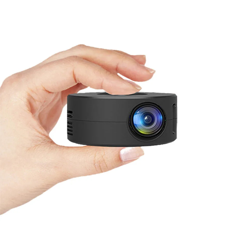 Black portable mini projector for children next to a mobile phone on a table.