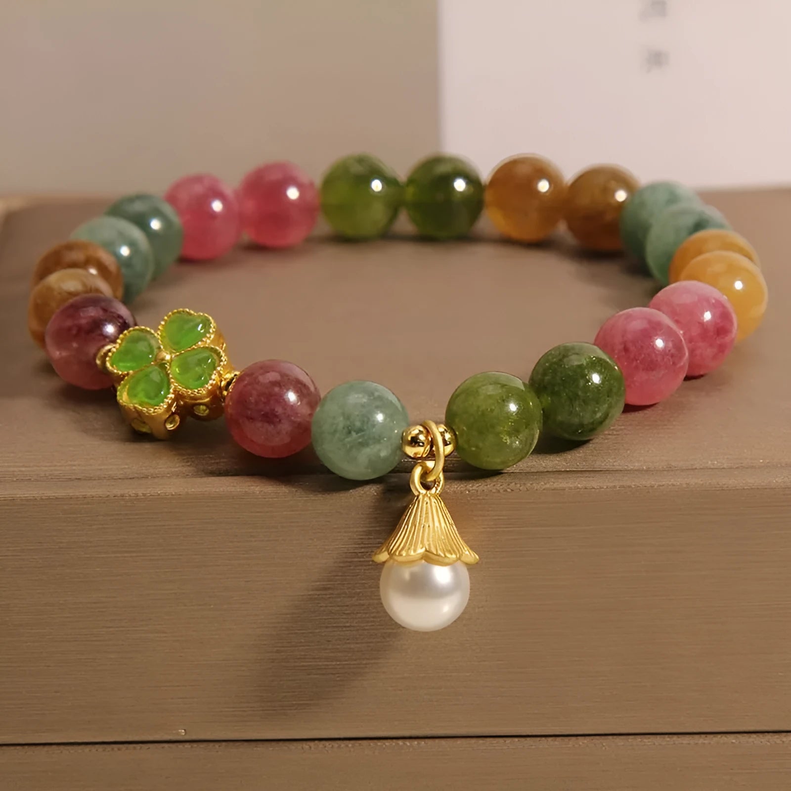 Natural colour tourmaline bracelet with four-leaf clover pearl pendant, geometric drop shape on woman's wrist.