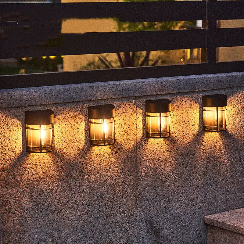Small solar-powered outdoor wall light with warm white glow, mounted on an exterior wall.