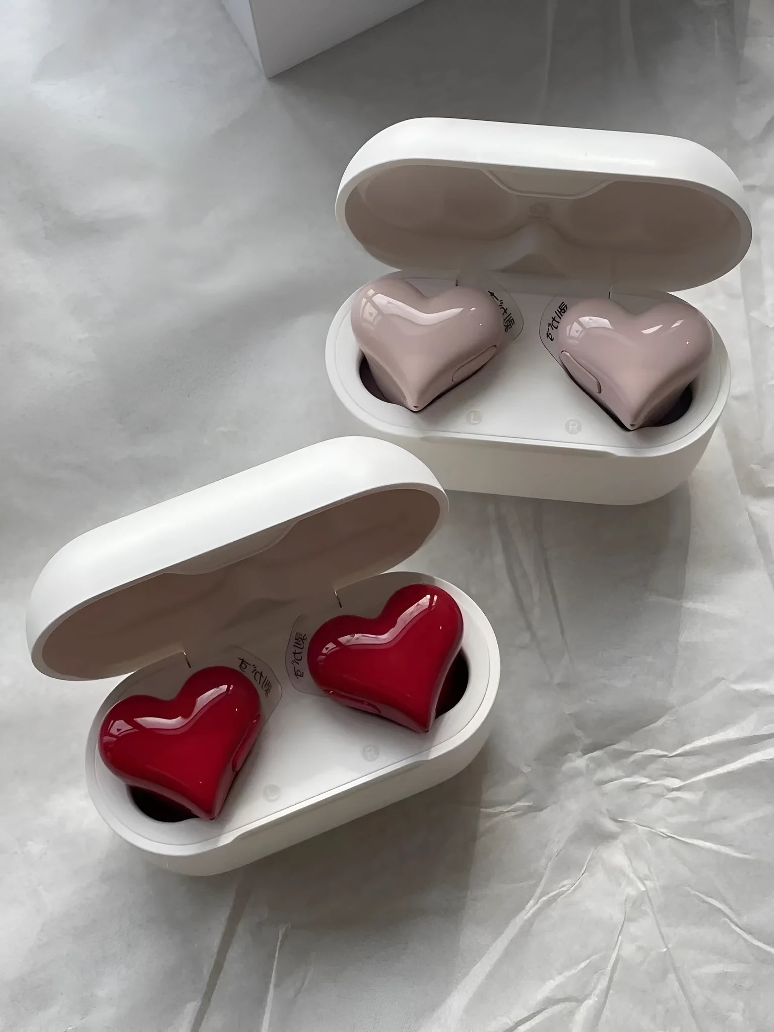 Heart-shaped wireless Bluetooth earbuds in red or pink colours with charging cable