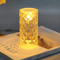 Rose atmosphere crystal bedside lamp with plastic lampshade emitting soft yellow light on a wooden table