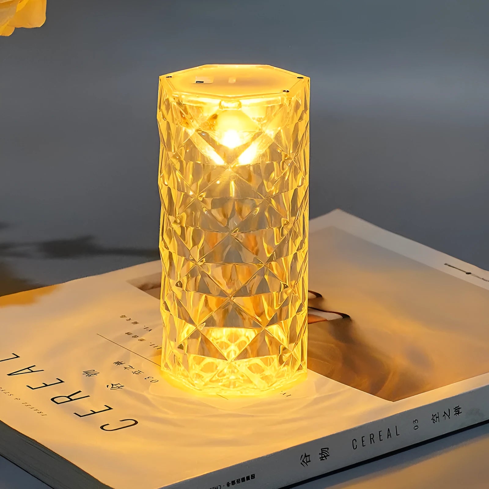 Rose atmosphere crystal bedside lamp with plastic lampshade emitting soft yellow light on a wooden table