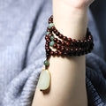 A wooden beaded bracelet with a carved green Hotian jade pendant on a natural background.