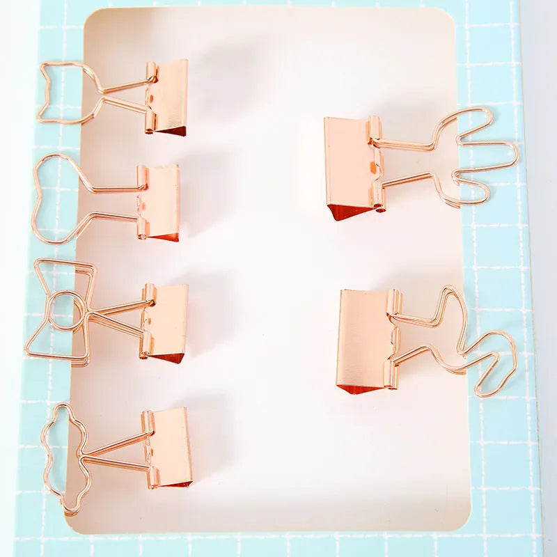 Gold metal paper clip with a long tail, showing decorative flamingo, love, cloud, cat, cactus, and bow motif options.