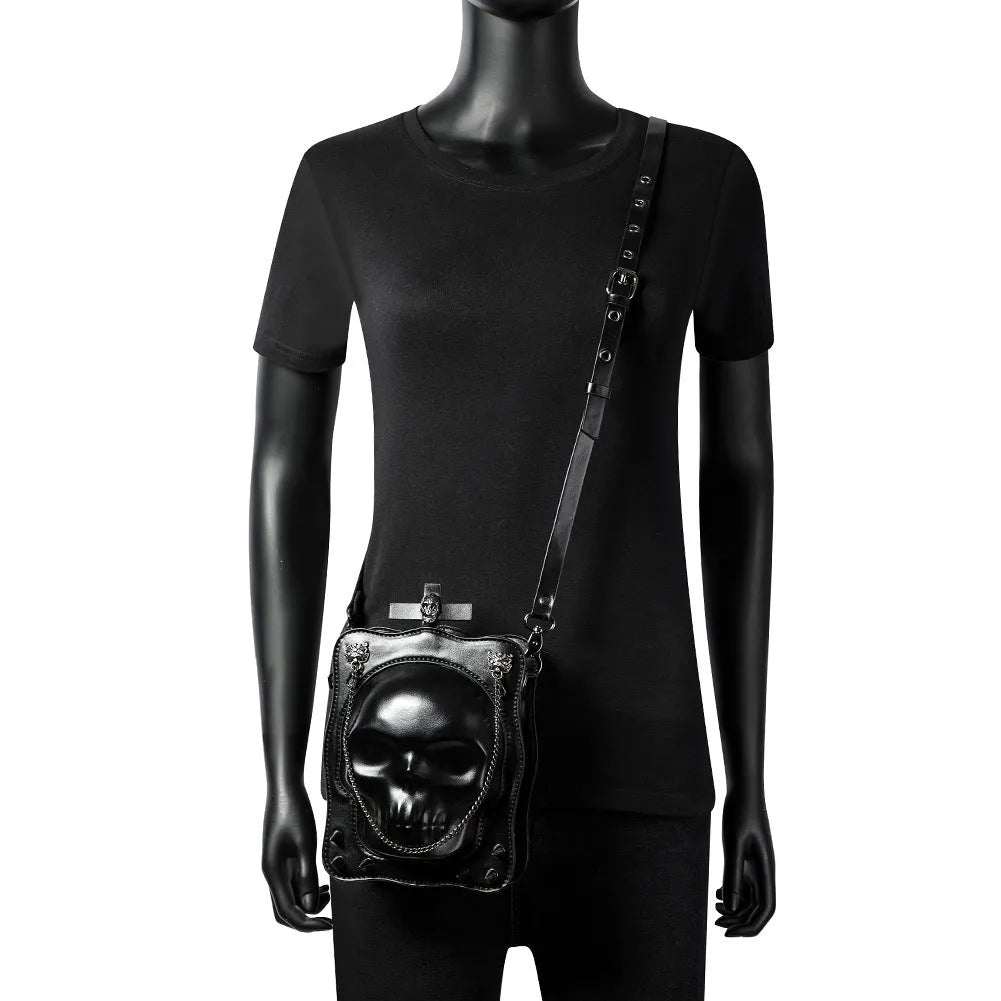 Black mini square crossbody bag with embossed skull design, metal rivets, chain strap, and top zipper.