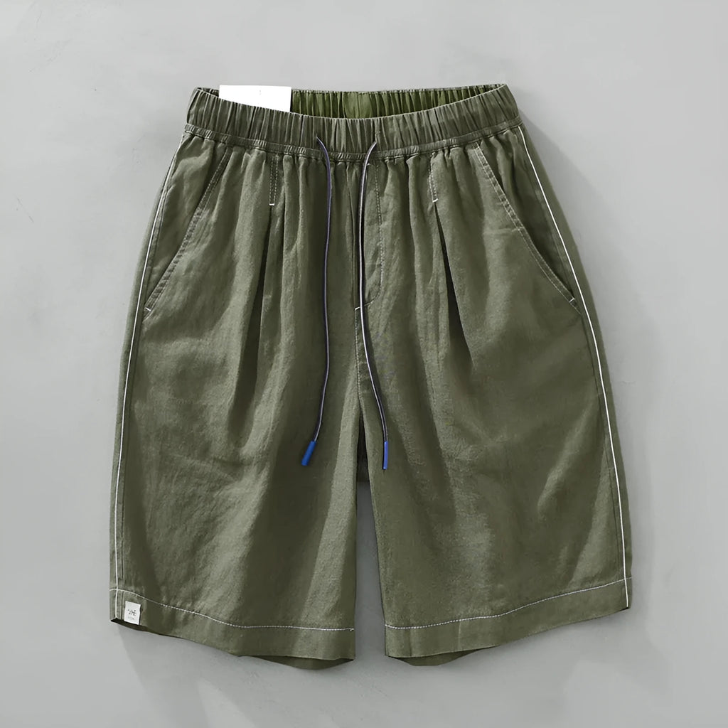 Man wearing loose straight-leg linen shorts in green, showcasing mid-waist and drawstring detail.
