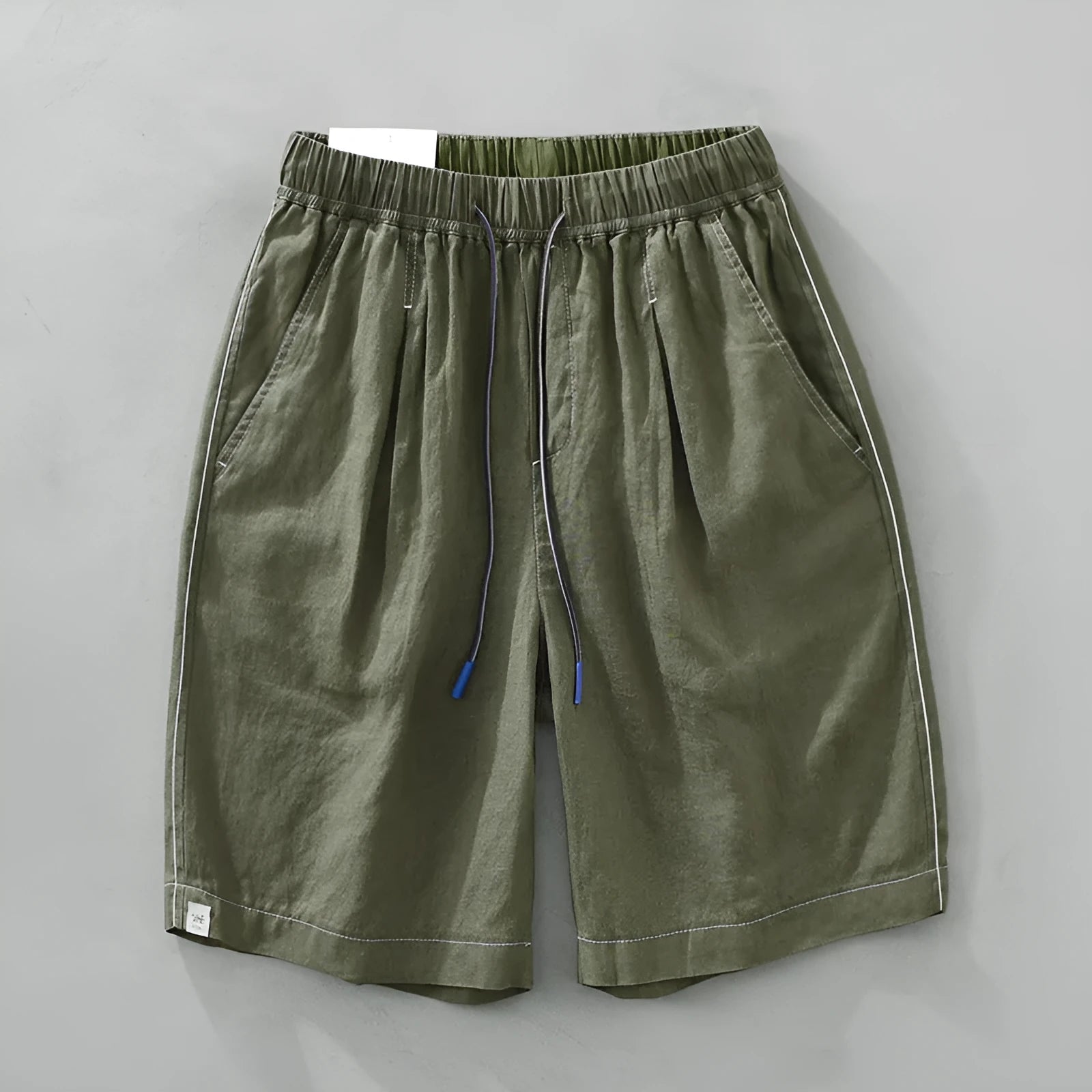 Man wearing loose straight-leg linen shorts in green, showcasing mid-waist and drawstring detail.