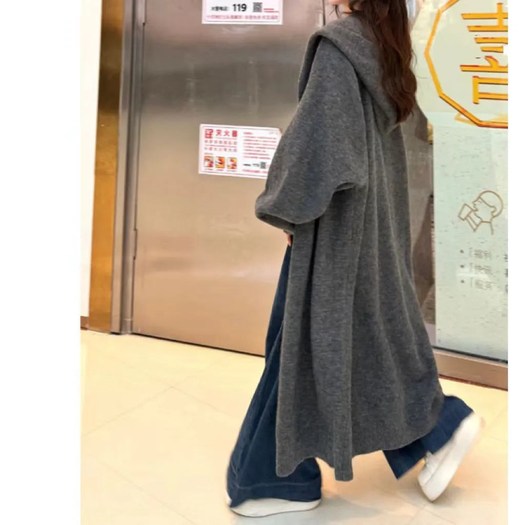 Long beige hooded knitted cardigan on a woman, showcasing its below-the-knee length and loose fit.