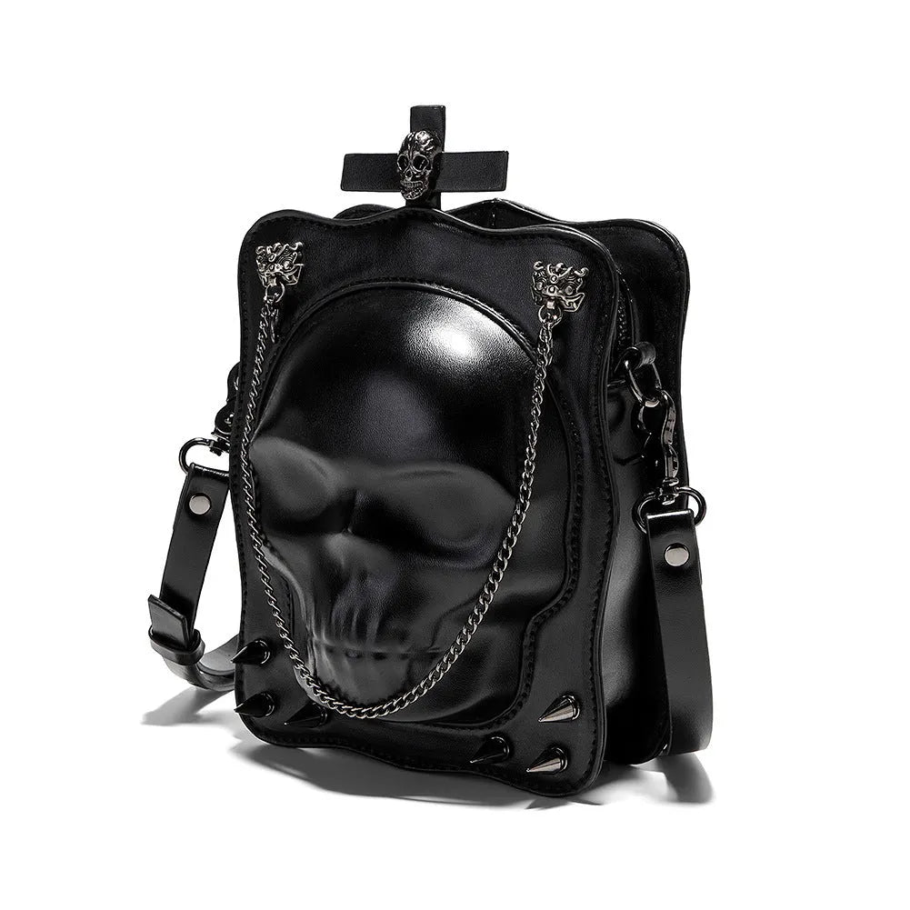 Black mini square crossbody bag with embossed skull design, metal rivets, chain strap, and top zipper.