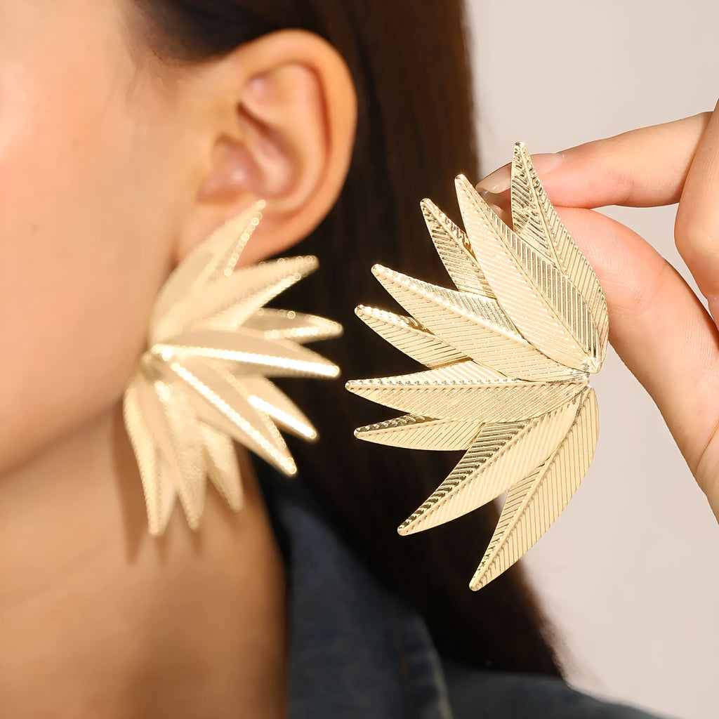 Gold and white alloy leaf shape patch earrings on a flat surface