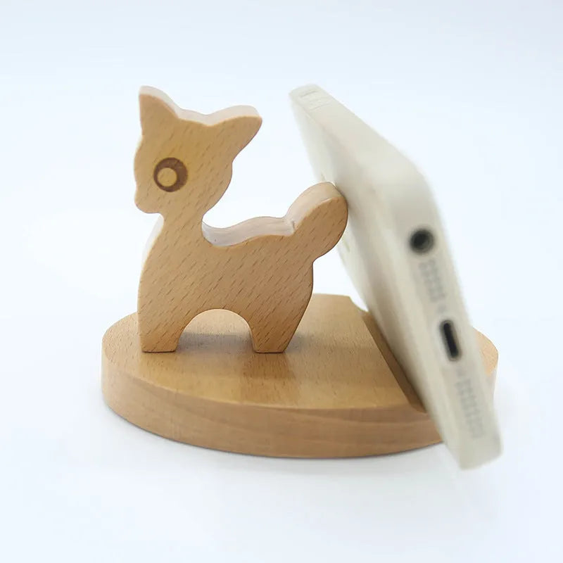Solid beech wood mobile phone stand with a resin cow figurine and a slot for holding coins on a wooden desk.