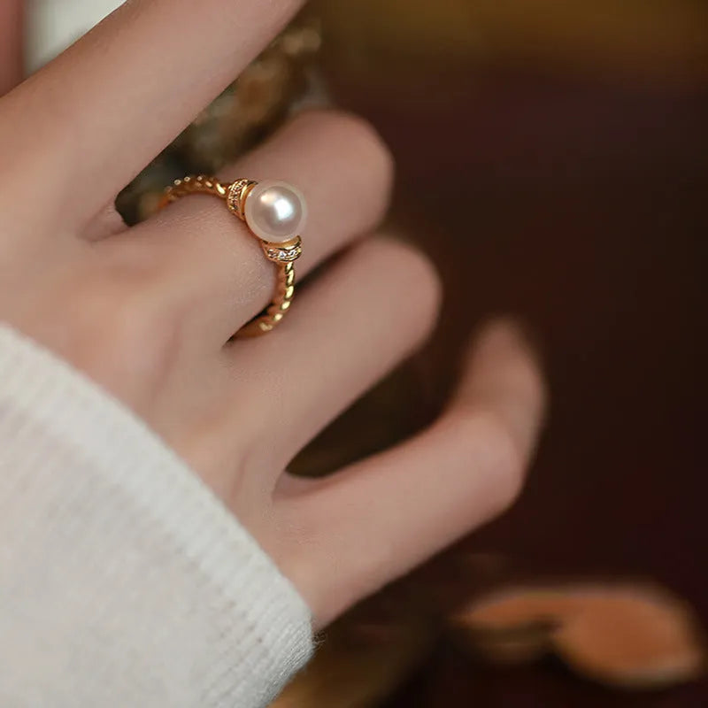 Adjustable geometric twist ring in copper with a central natural pearl on a model's finger.