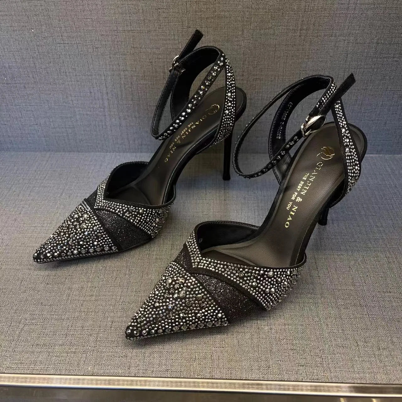Women's black hollow high heel shoe with red sole, stiletto heel, and pointed toe on a plain background.