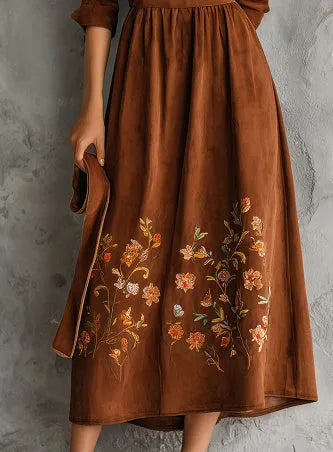 Brown suede-effect midi dress with detailed floral embroidery on the skirt, shown on a model.