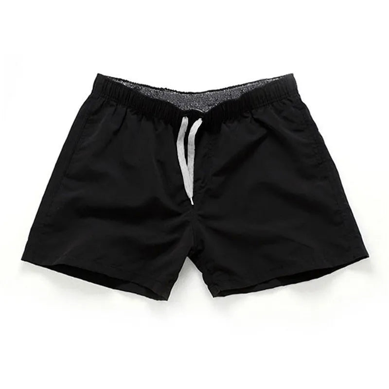Men's straight-leg polyester surf shorts on a beach, showing colour options like black, fluorescent yellow, and navy blue.