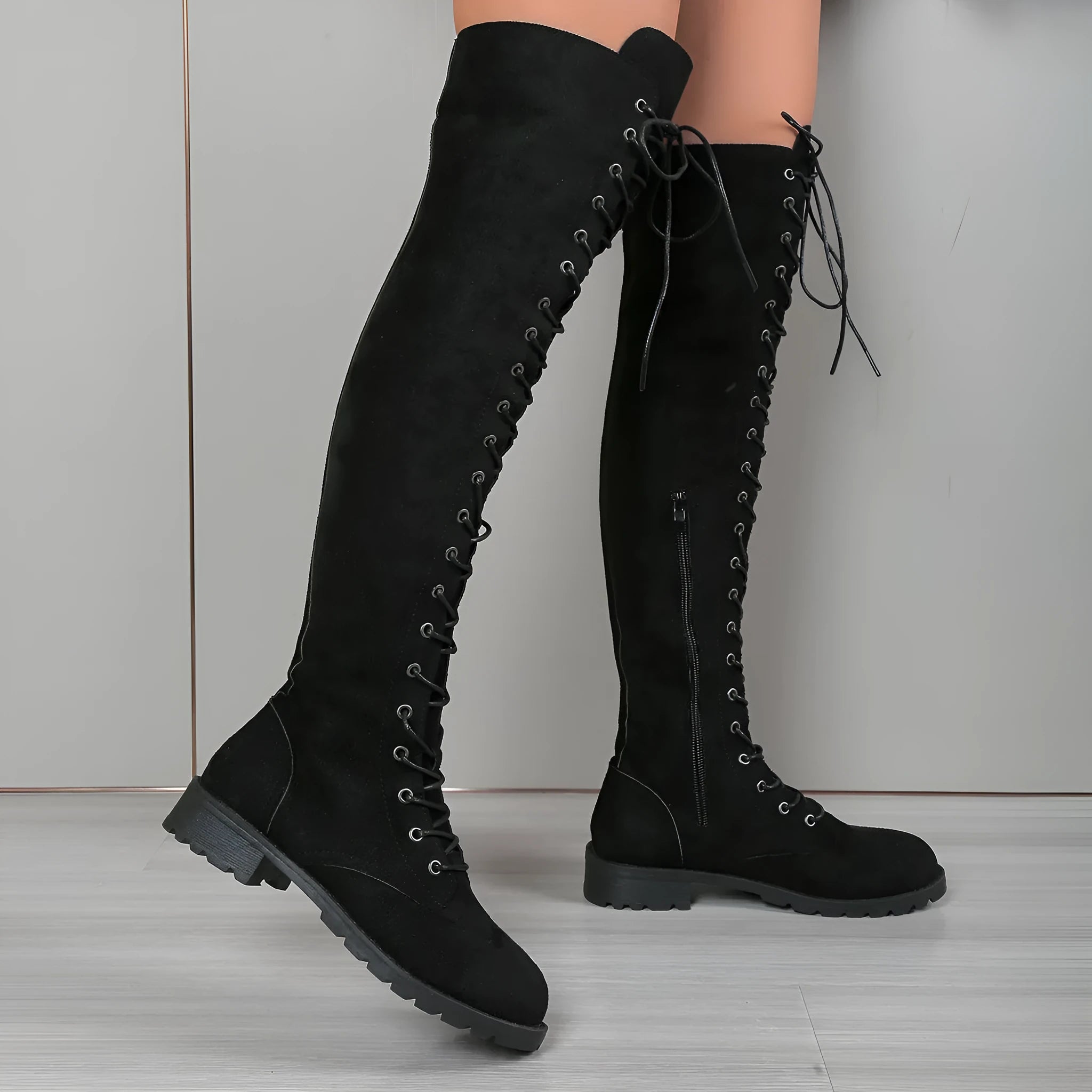 Black lace-up over-the-knee boots with decorative stitching, a round toe, and a flat rubber sole on a neutral background.