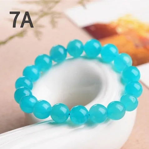 A selection of loose, polished ice-blue Amazonite beads in various sizes next to a finished crystal bracelet.