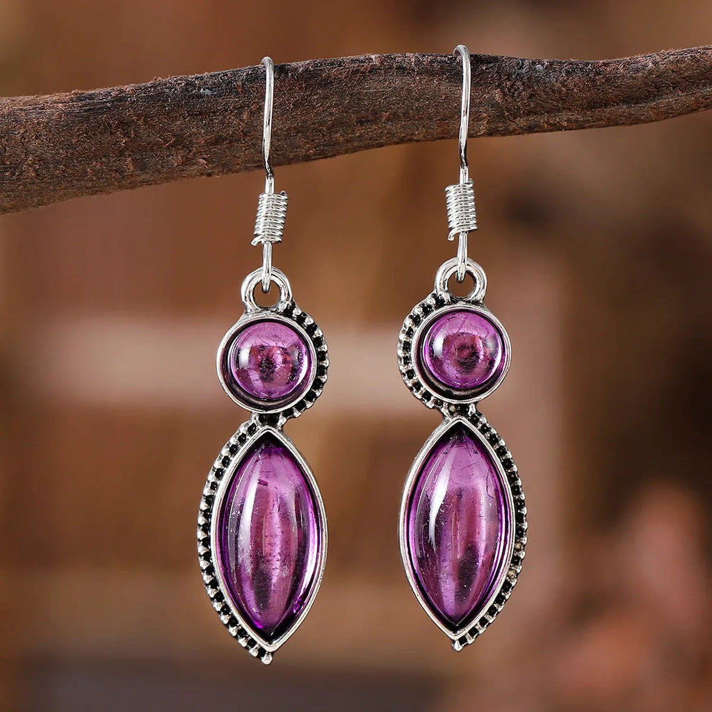 Vintage silver-tone geometric drop earrings with round purple and black stones on a grey background.