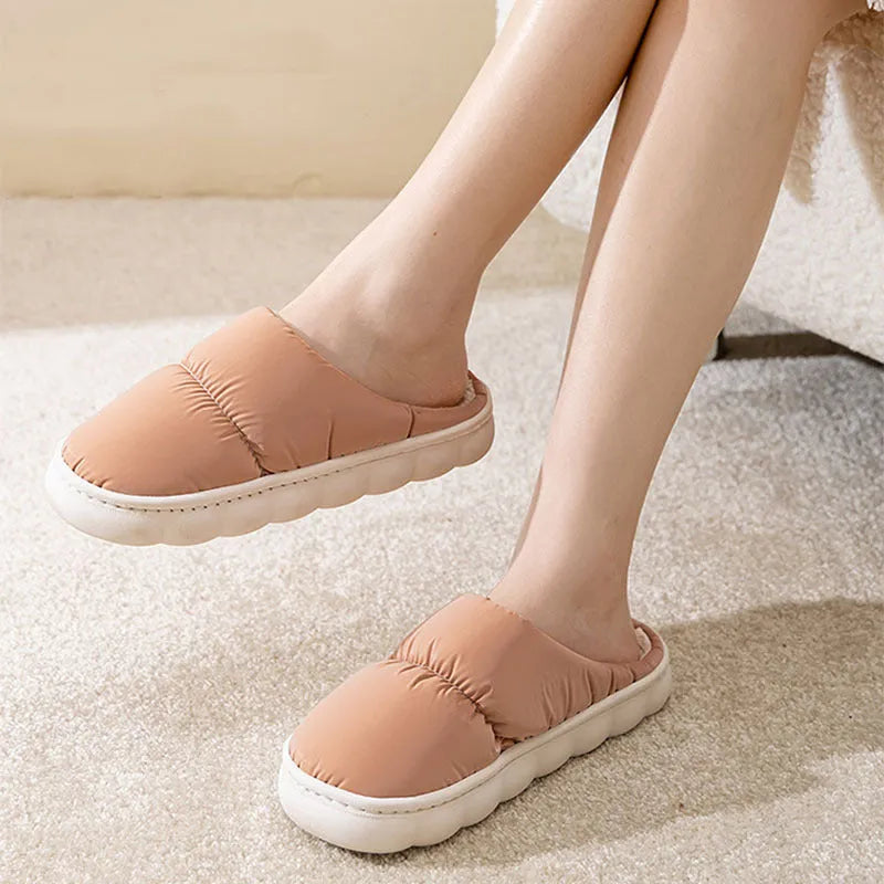 A pair of blue down cotton winter slippers with a thick rubber sole and plush lining on a wooden floor.