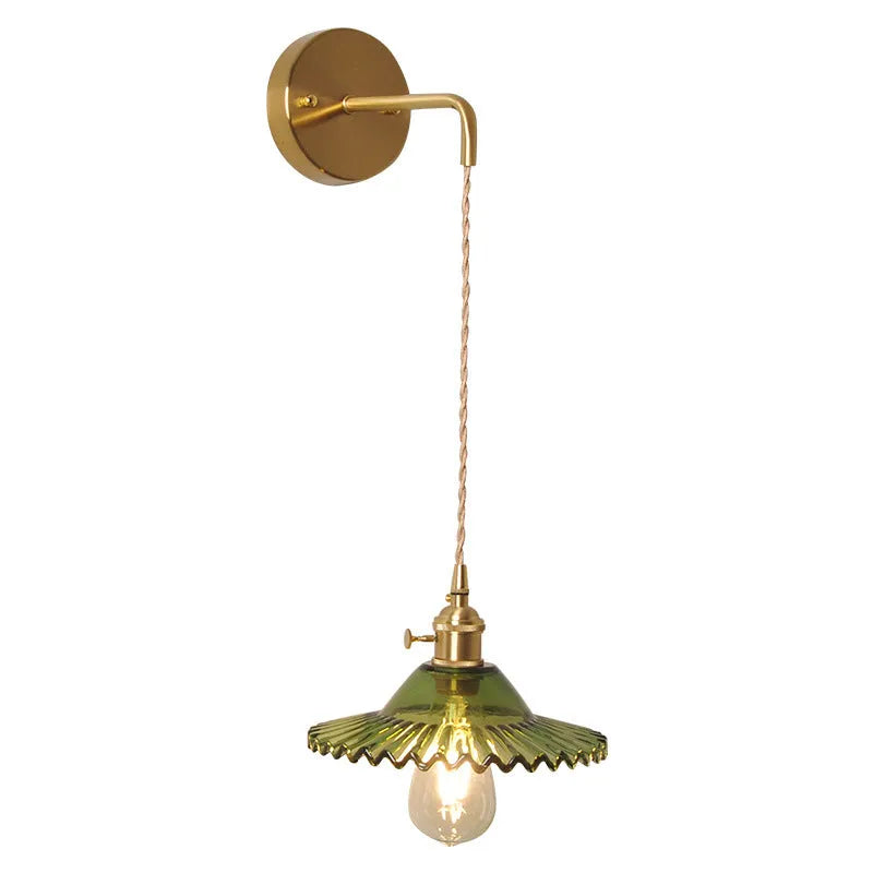 Retro brass lotus wall lamp with a 22cm green glass shade mounted on a copper base beside a bed.