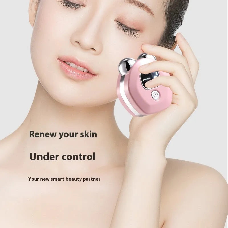 Portable white facial massager with hot compress function and double-roller head on a pink background.