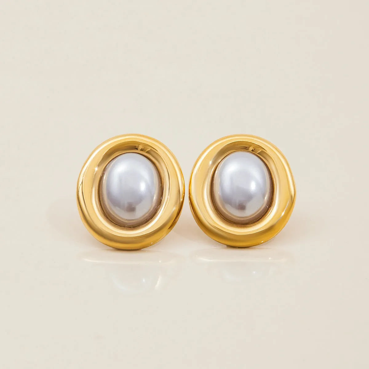 A pair of small stainless steel ear studs with a vintage-style pearl decoration on a silver-coloured base.