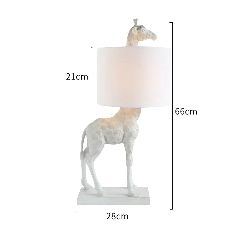 White or gold giraffe-shaped table lamp with cloth shade on a bedside table.