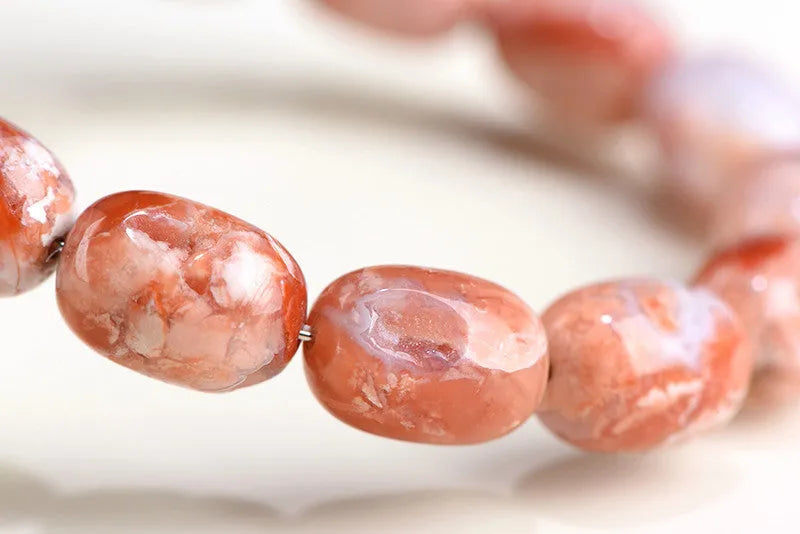 Natural cherry agate barrel bead bracelet with Ruyi symbols on a white background.