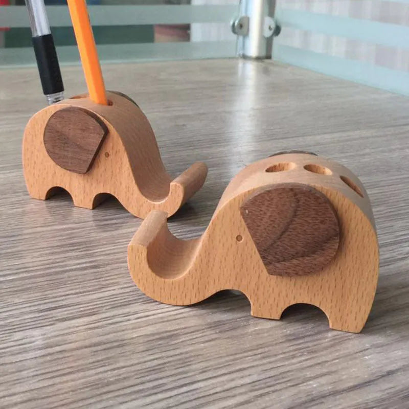 Solid beech wood mobile phone stand with a resin cow figurine and a slot for holding coins on a wooden desk.