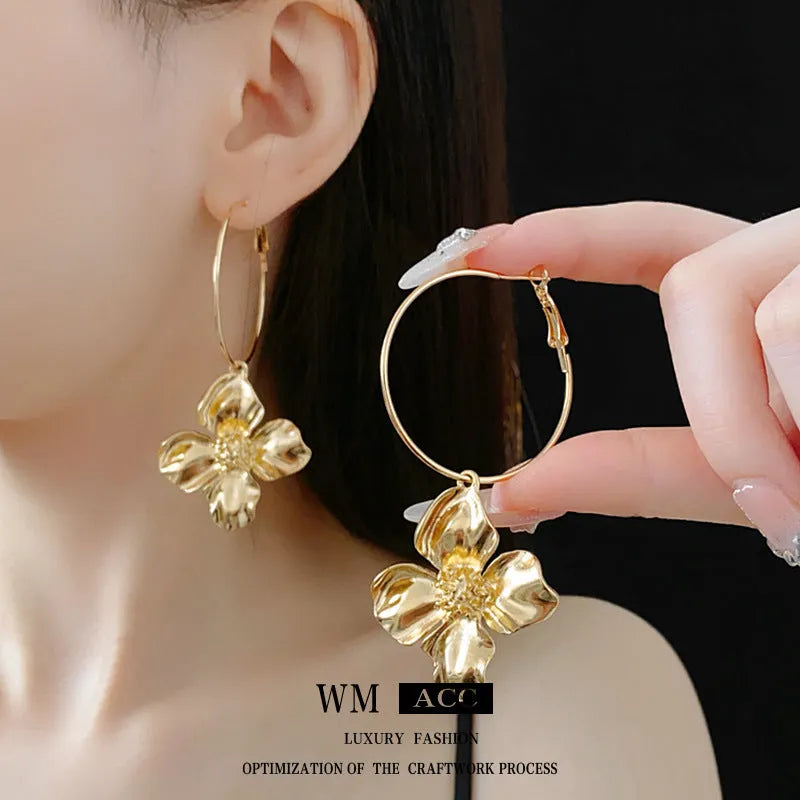 A pair of geometric flower-shaped metal earrings with a silver needle detail, shown in gold and silver electroplated finishes.