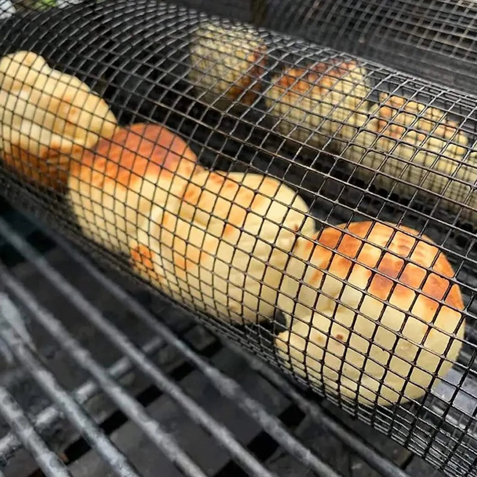 Stainless steel cylindrical rolling barbecue grilling basket with wire mesh on a grill.