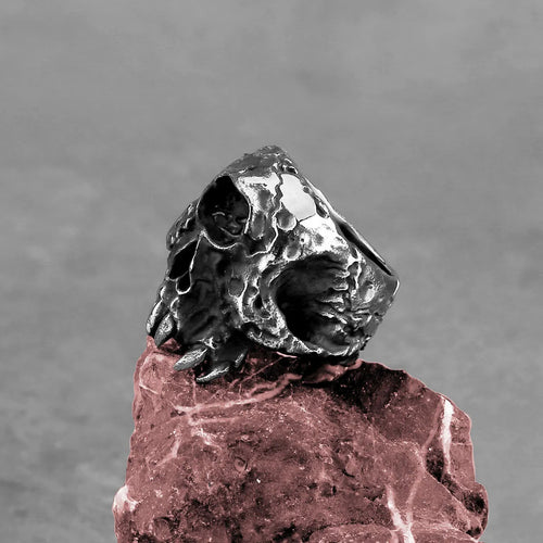 A silver-toned alloy ring featuring a detailed one-eyed skull design on a black background.