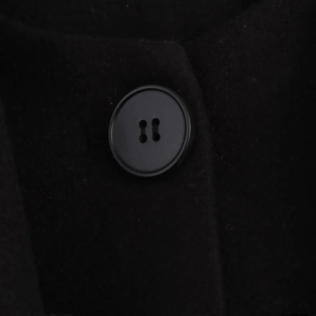 Women's long black coat with a grey artificial fur collar and side pockets, shown in a street fashion setting.