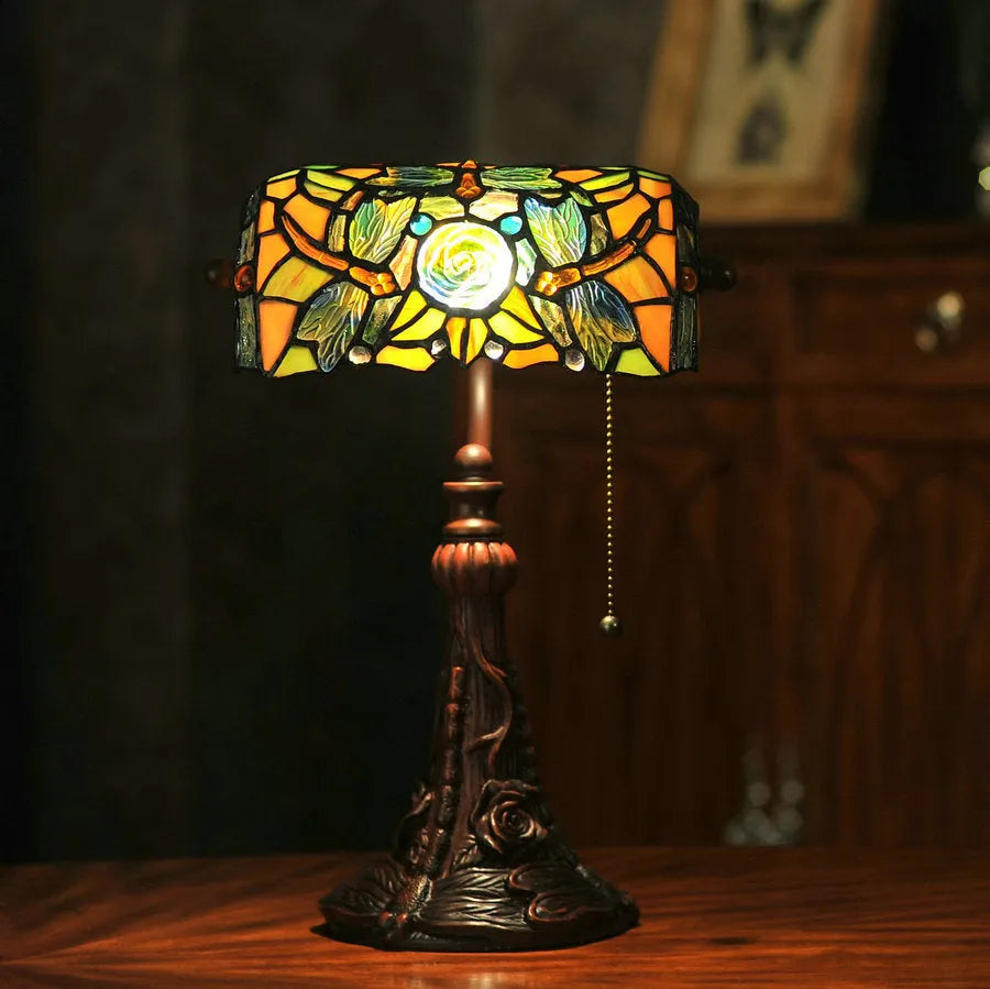Tiffany style table lamp with coloured stained glass shade and resin base on a desk.
