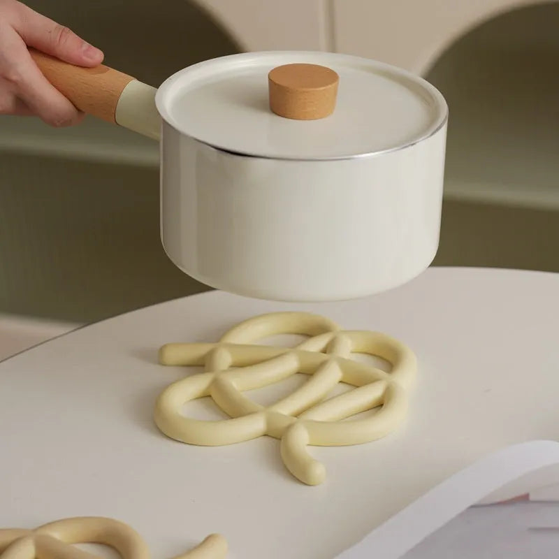 Modern irregular-shaped ceramic heat proof mat in grey protecting a wooden dining table from a hot pan.